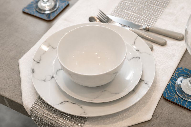Place setting with white bowls, plates, cutlery and marble-patterned napkin on table