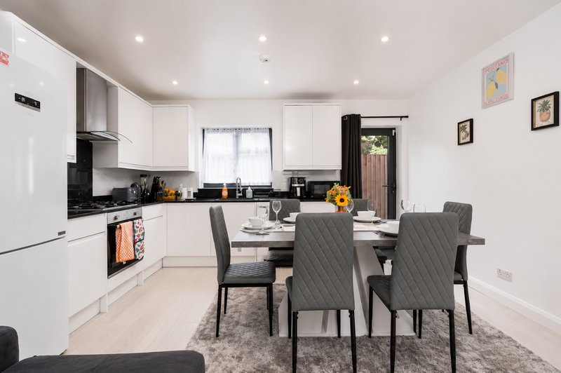 Modern open-plan kitchen and dining area with white cabinetry, black countertops, dining table and grey chairs