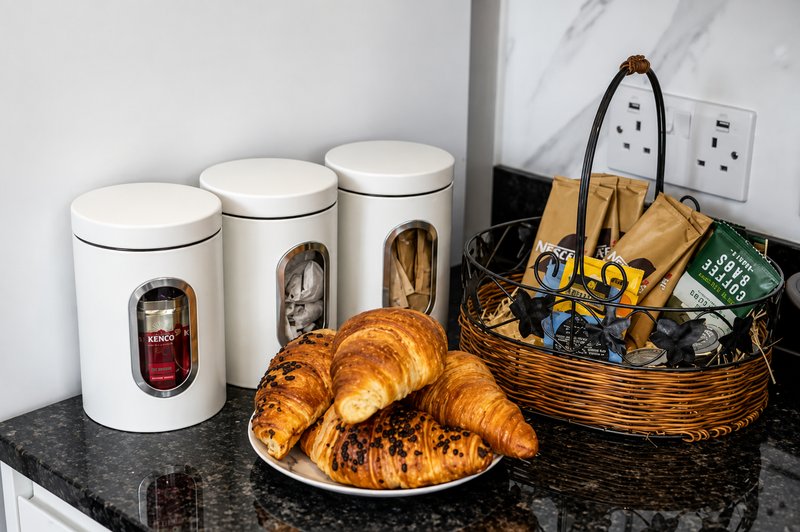 Kitchen counter with white storage canisters, fresh croissants on plate, and wicker basket with supplies