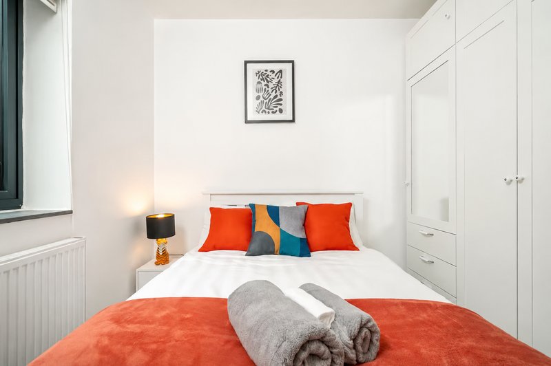 Modern bedroom with double bed, orange bedding, colorful pillows and white built-in wardrobes