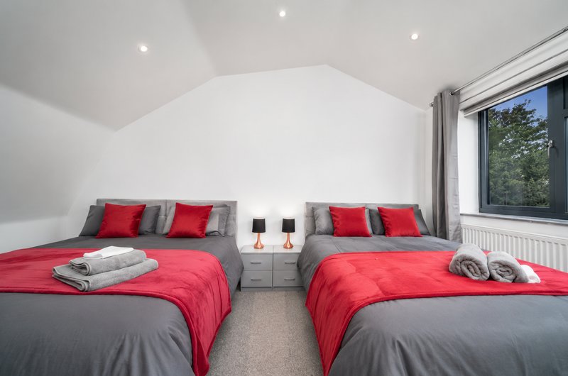 Modern bedroom with two double beds, red and grey bedding, twin bedside tables and large window