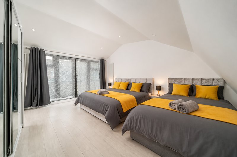 Modern attic bedroom with two beds, grey and yellow bedding, sloped white ceiling and large windows