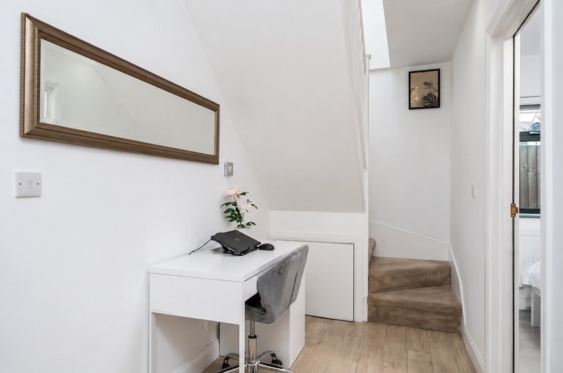 Bright hallway with white walls, wooden mirror, small desk, staircase and potted plant