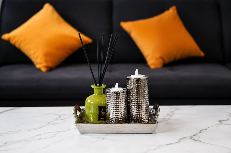 Living room detail with black sofa, orange cushions, and decorative table arrangement with candles and diffuser