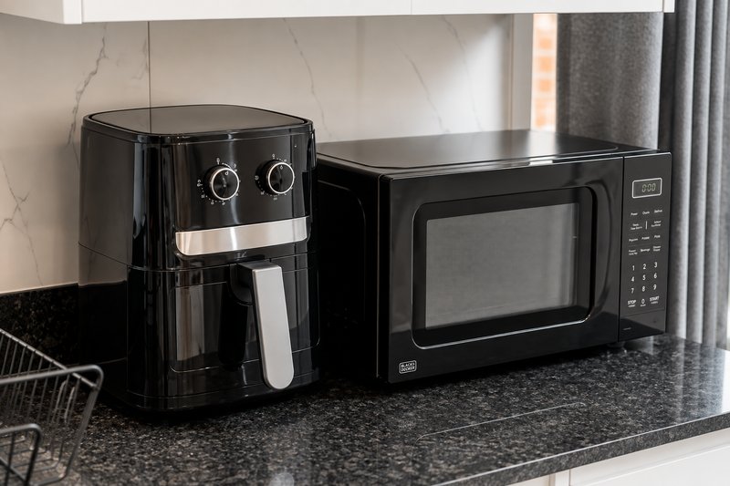 Kitchen counter with black air fryer and microwave oven, marble backsplash