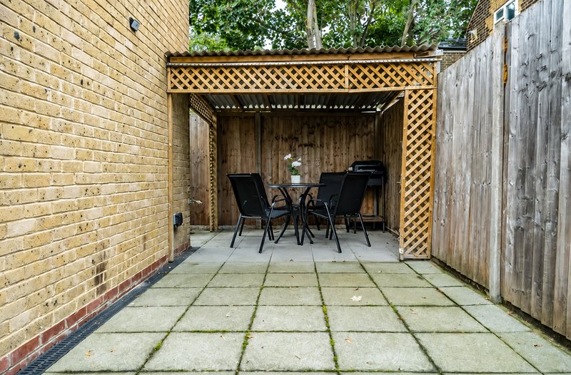Covered patio area with black chairs, wooden lattice roof, brick walls and paved flooring