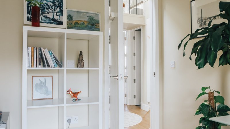 Bright hallway with white shelving unit displaying books, artwork, plants and decorative items