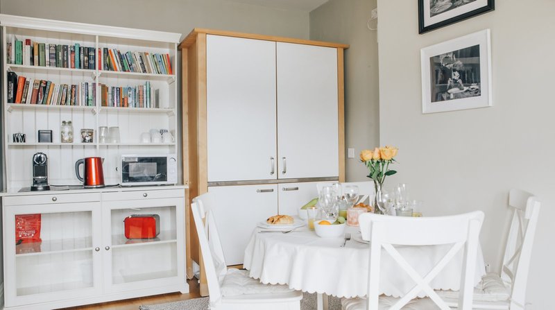 Bright dining area with white round table, chairs, built-in bookshelf and kitchen cabinetry