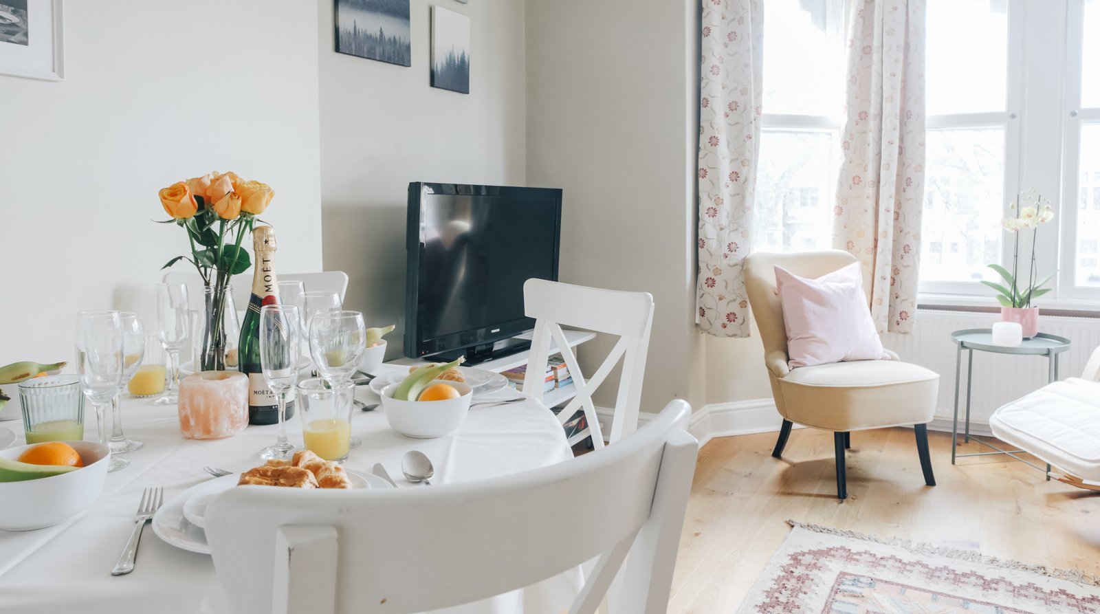 Open-plan dining and living room with white furniture, orange flowers, and bright windows