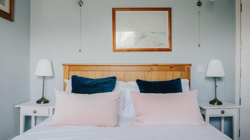 Bedroom with double bed, wooden headboard, pink pillows, navy cushions, white nightstands and lamps