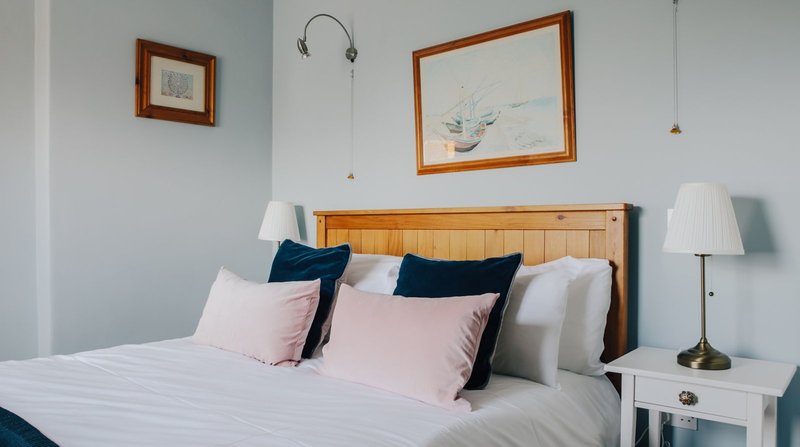 Bright bedroom with wooden headboard, pink and navy cushions, white bedding, and bedside lamps