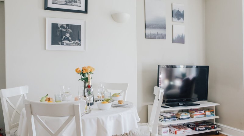 Bright dining area with round white table, chairs, flowers, TV, and framed wall art