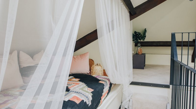 Bedroom with canopied bed, white curtains, decorative pillows and potted plant on shelf
