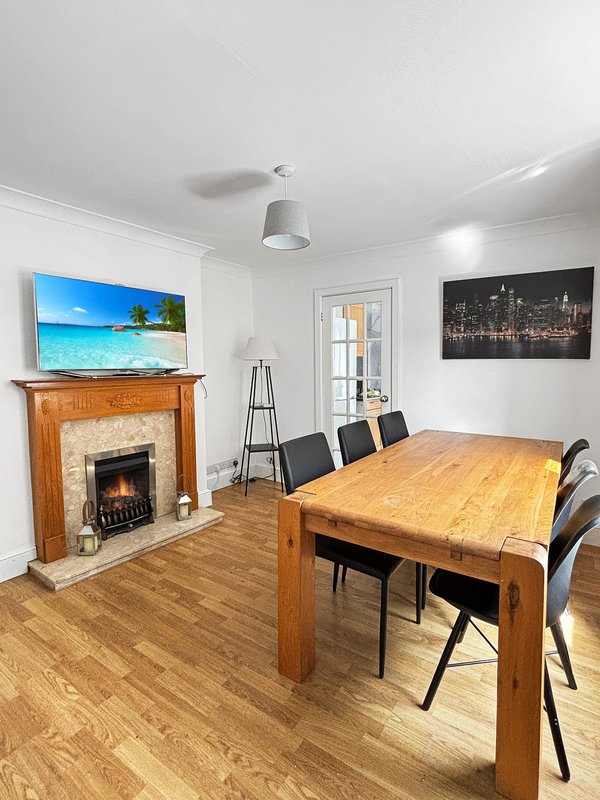 Open-plan living and dining room with wooden table, fireplace, TV and modern chairs