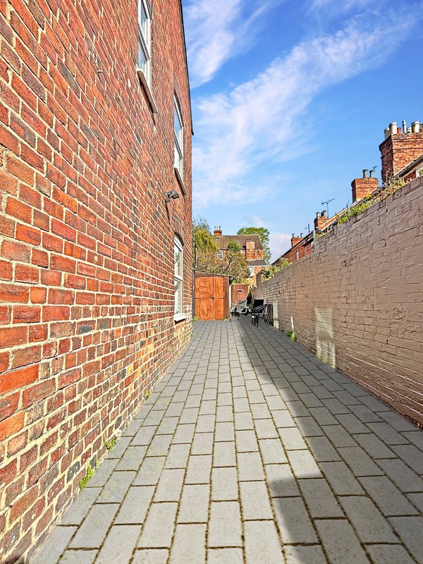 Narrow brick alleyway between red and grey brick walls with paved ground