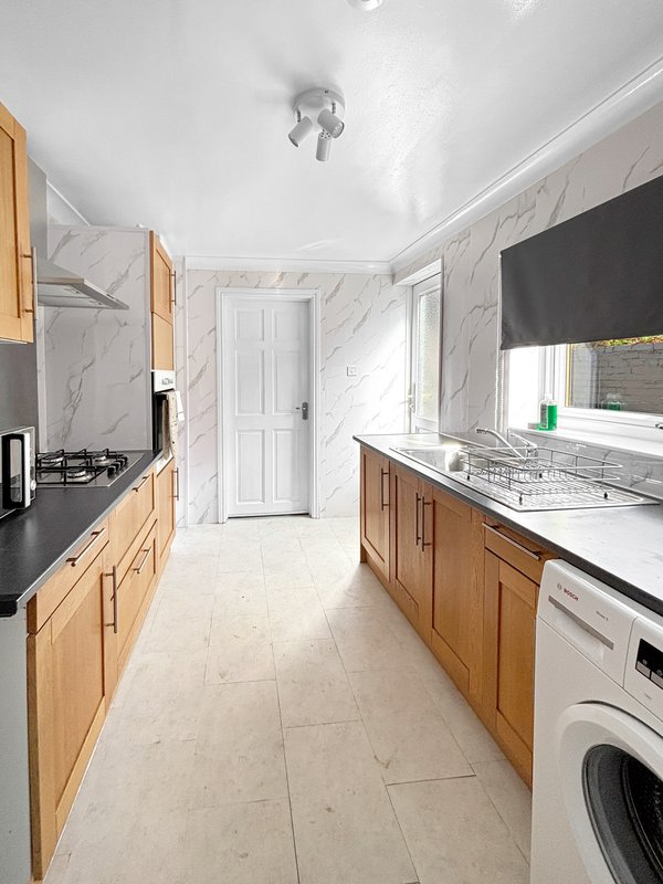 Modern galley kitchen with wooden cabinets, marble-effect walls, white appliances and island