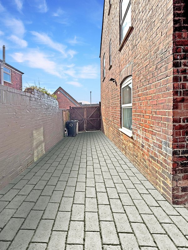 Side alleyway with paved ground, brick walls, wooden gate and blue sky