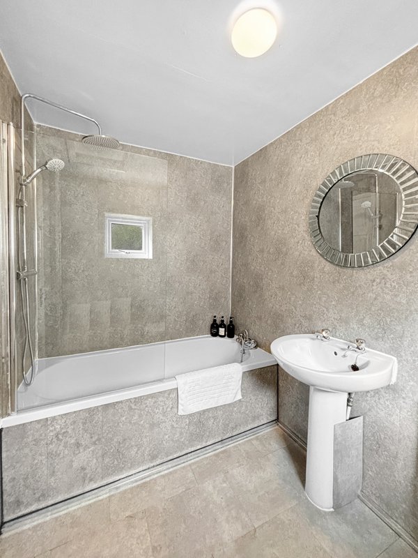 Modern bathroom with bathtub, pedestal sink, round mirror and ceiling light