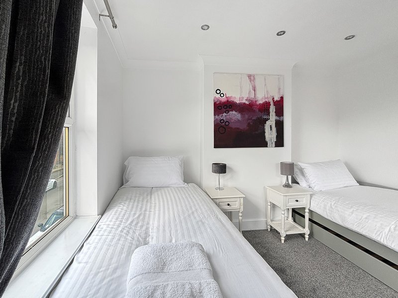 Twin bedroom with single beds, white bedding, nightstands, and abstract wall art