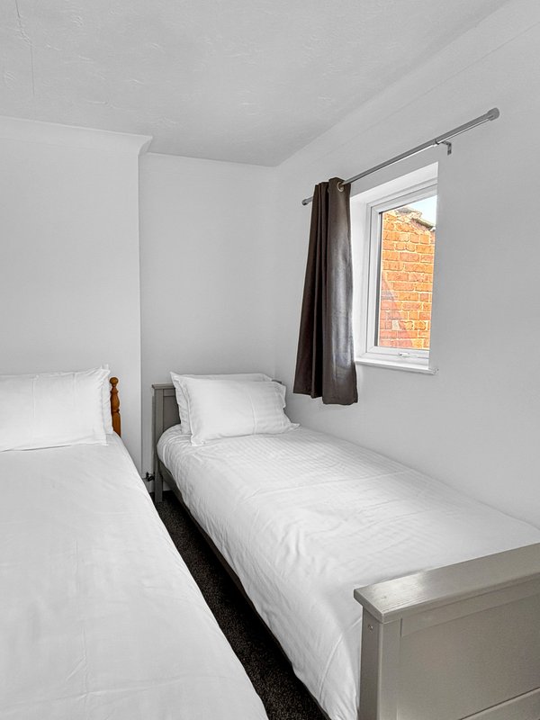 Bright bedroom with two single beds, white bedding, window with brown curtains and brick view