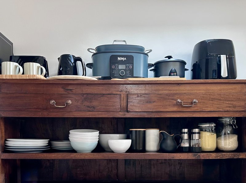 Kitchen shelving unit displaying small appliances, dishware, bowls, and storage containers