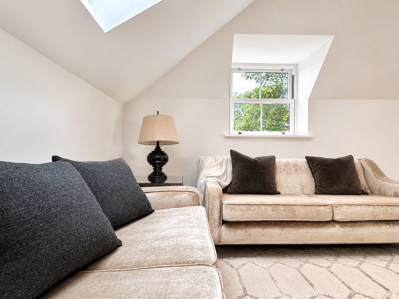 Bright attic bedroom with two sofas, black lamp, skylight windows and neutral decor