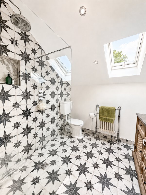 Modern bathroom with star-patterned tile floor, shower enclosure, toilet, heated towel rail and skylight