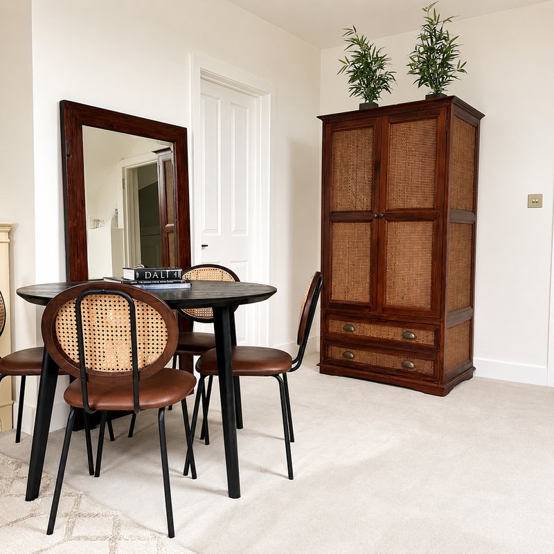 Bright dining area with round black table, rattan chairs, wooden wardrobe and mirror