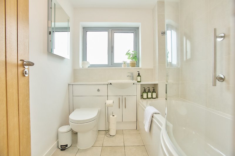 Clean bathroom with toilet, vanity sink, mirror, window and bathtub
