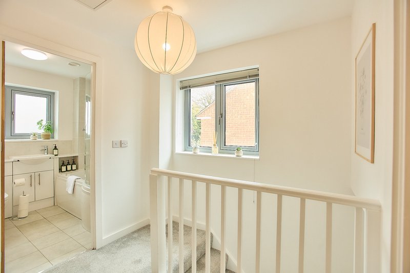 Bright hallway with pendant light, white bannister, bathroom visible, and window