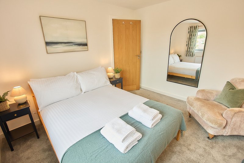 Bedroom with double bed, white bedding, wooden door, arched mirror and comfortable seating area