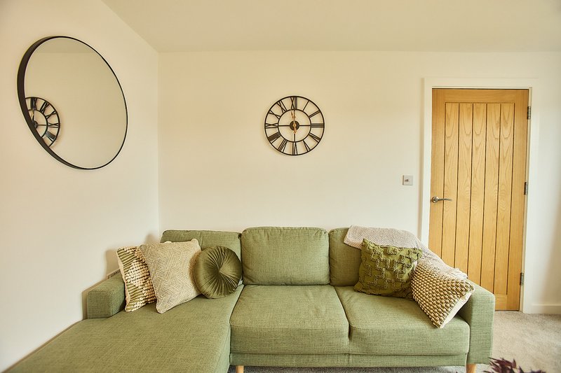 Living room with green corner sofa, decorative wall clocks, and wooden door