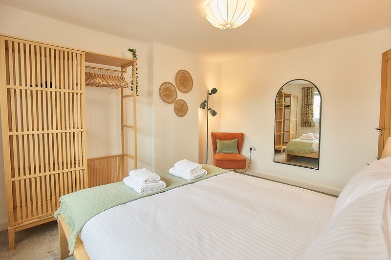 Bright bedroom with double bed, wooden furniture, mirror, and modern decor