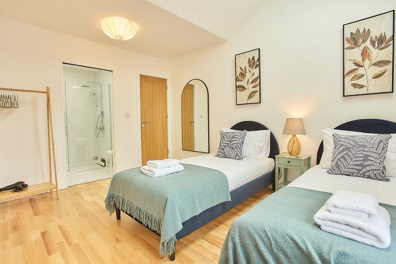 Bright bedroom with two single beds, wooden floor, ensuite bathroom and botanical wall art