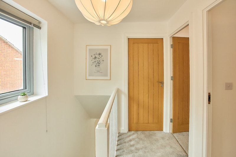 Bright hallway with white walls, wooden doors, pendant light and staircase railing
