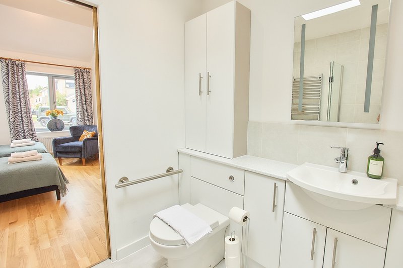 Modern white bathroom with toilet, vanity sink, mirror and access to bedroom beyond