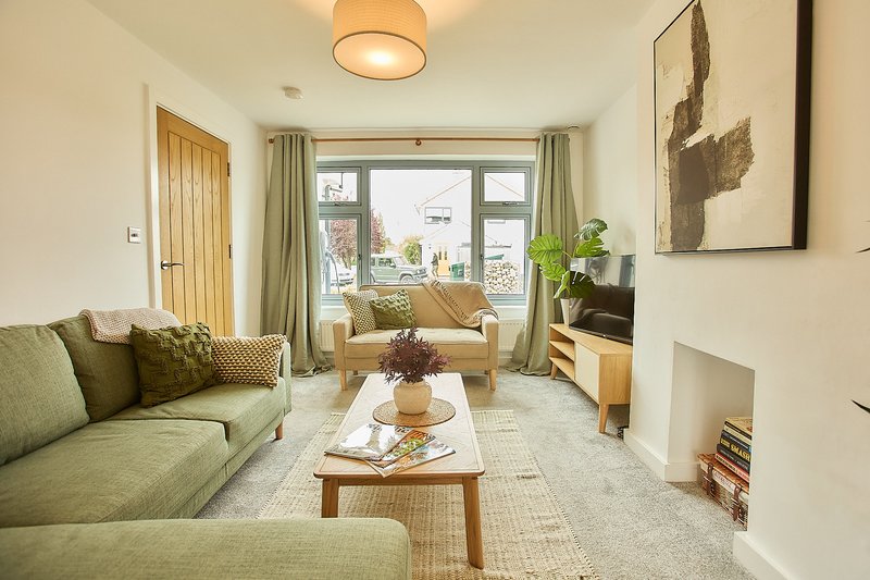 Bright modern living room with green sofa, wooden furniture, and glass doors opening to garden