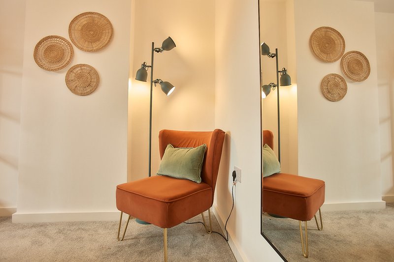 Modern living room with orange accent chair, floor lamp, woven wall baskets, and mirror