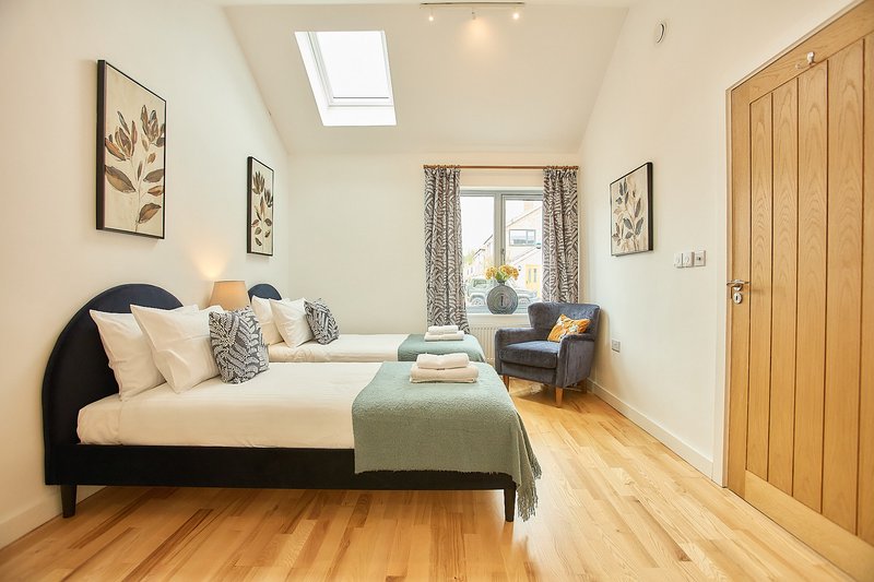 Bright bedroom with double bed, wooden floor, armchair, and botanical wall art