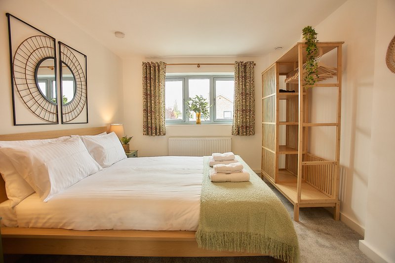 Bright bedroom with wooden bed, white bedding, green throw, wooden shelving unit and window with curtains