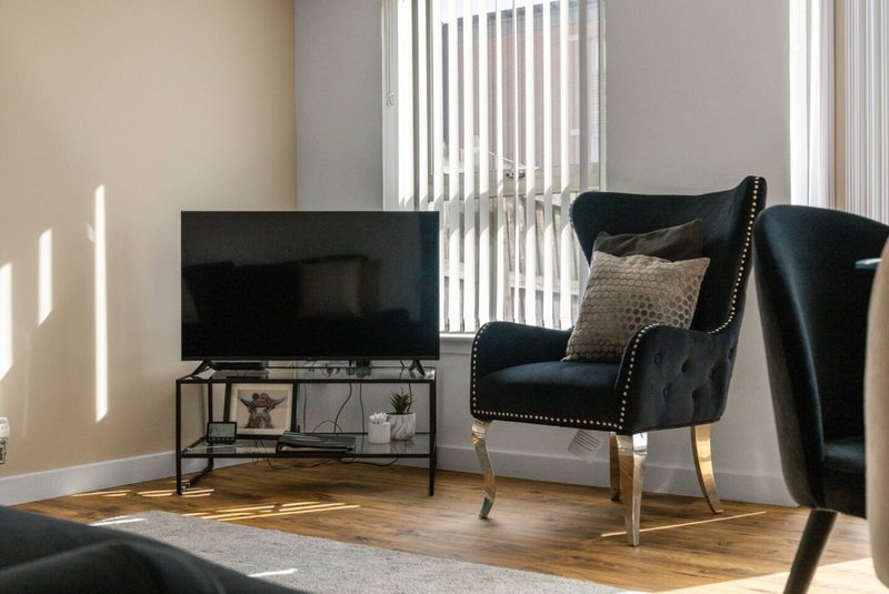 Living room with black leather armchair, TV stand, and wooden flooring near windows