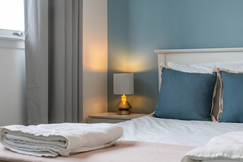 Modern bedroom with double bed, blue cushions, bedside lamp and folded towels