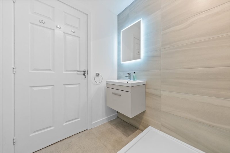 Modern bathroom with illuminated mirror, floating vanity, white door and light wood wall paneling