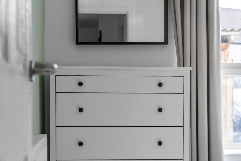 Bedroom with white dresser, mirror, window with curtains and green accent wall