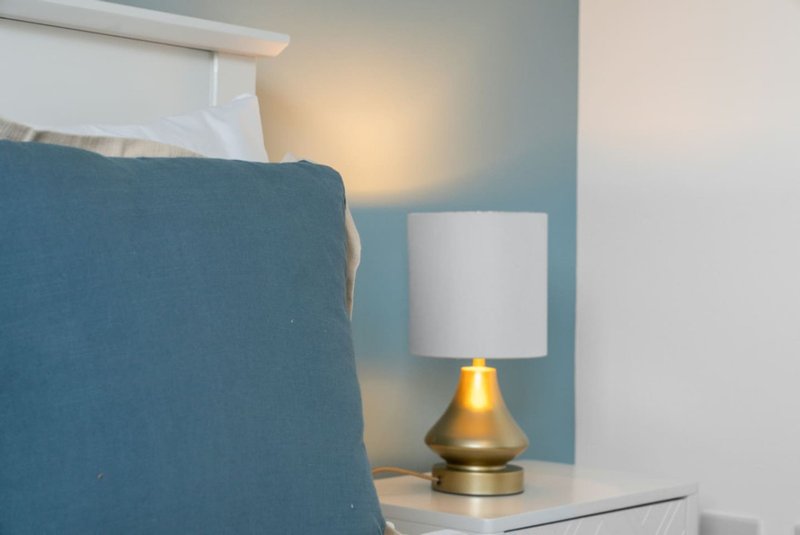 Bedroom corner with blue upholstered chair, white bedside table and brass table lamp