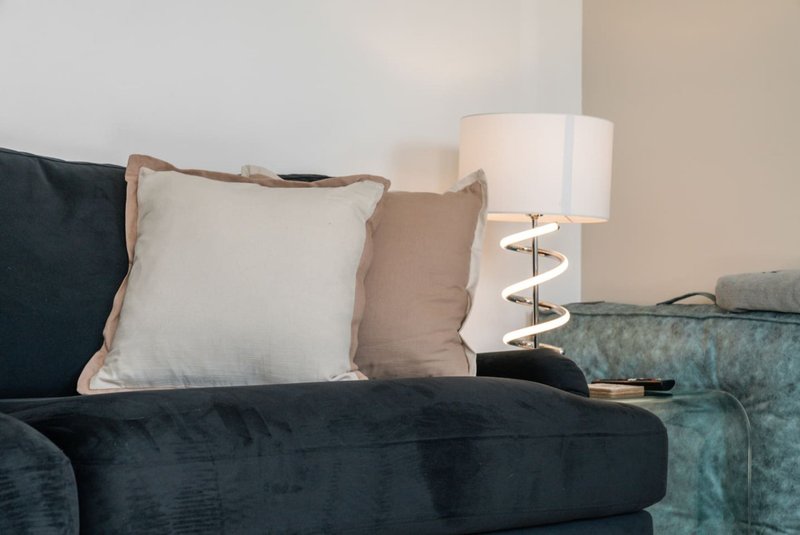 Living room corner with dark sofa, decorative pillows, and table lamp with spiral base