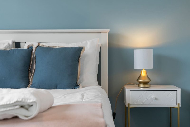 Modern bedroom with blue cushions, white bedding, brass lamp and bedside table