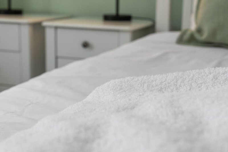 Close-up of white bedding on bed with white nightstands and green headboard visible