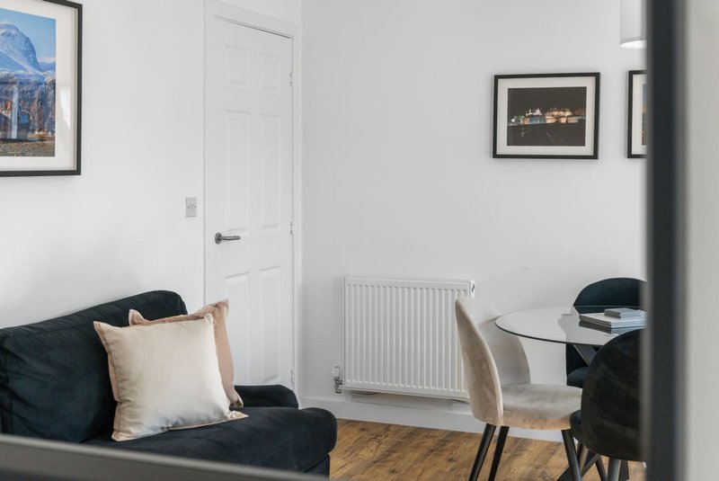 Modern living room with black sofa, dining table, white door and framed wall art