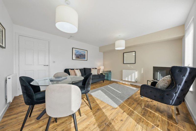 Modern living room with black leather sofa, white dining table, wooden floor and pendant lighting